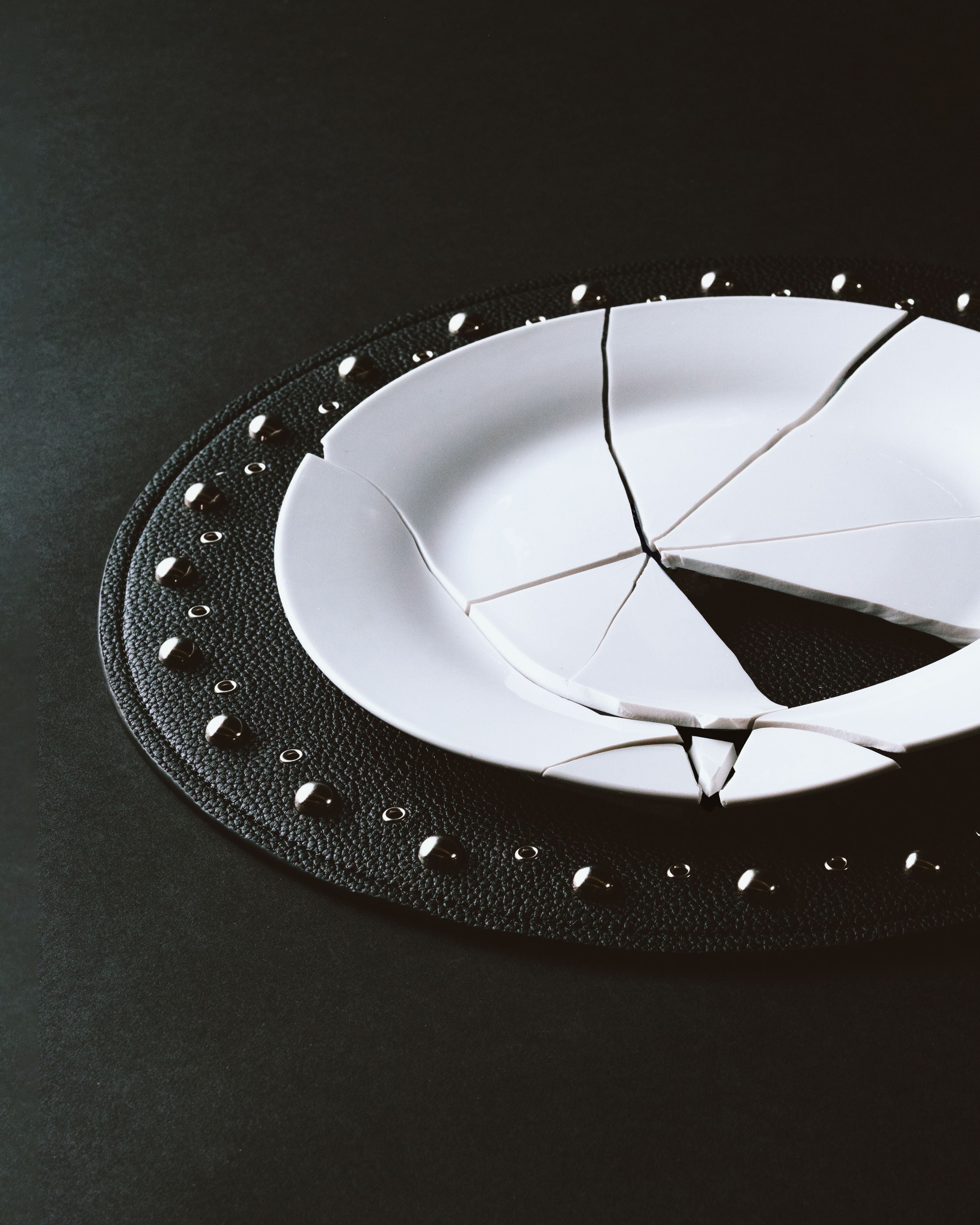 Broken white ceramic plate on black studded recycled leather placemat