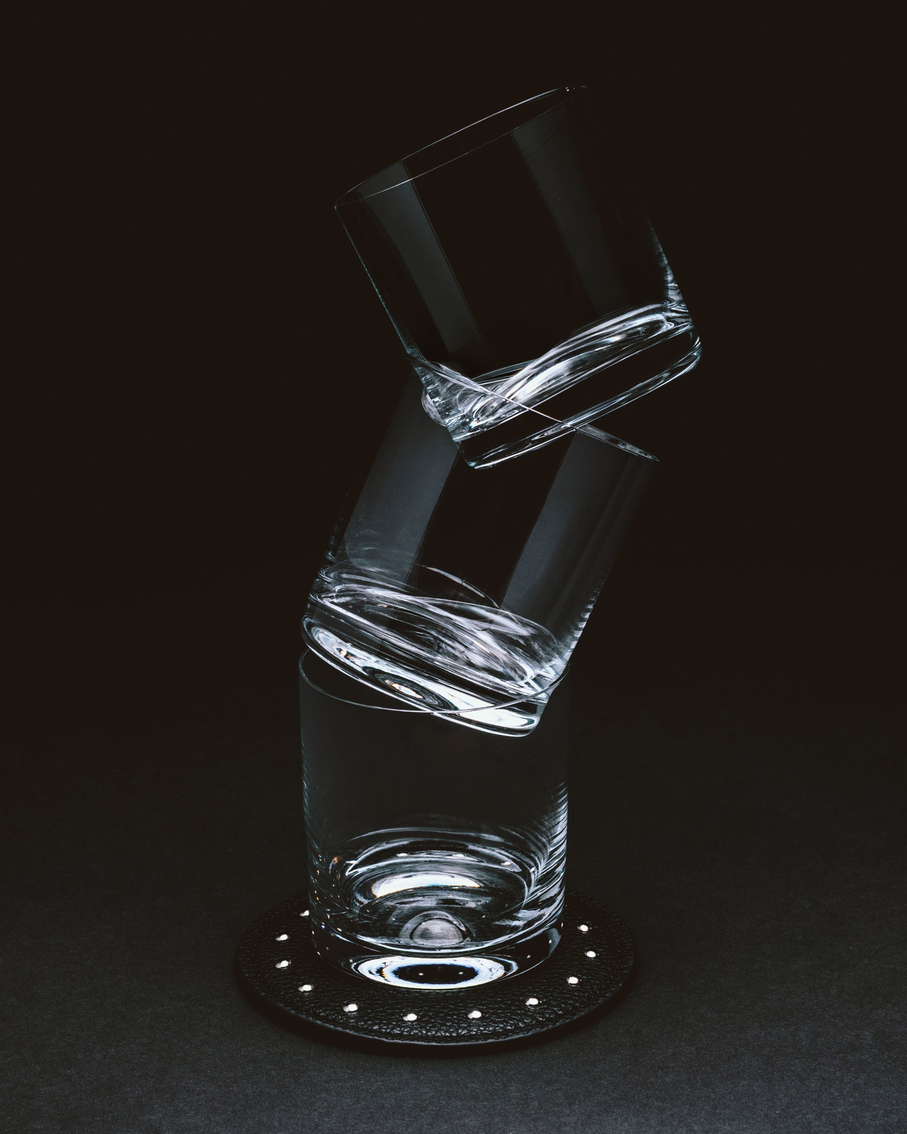 Stacked crystal glasses balanced on black studded recycled leather coaster